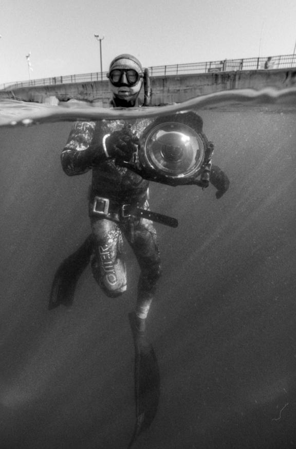 Artist Ryuijie with his underwater camera in a dive suit in water.